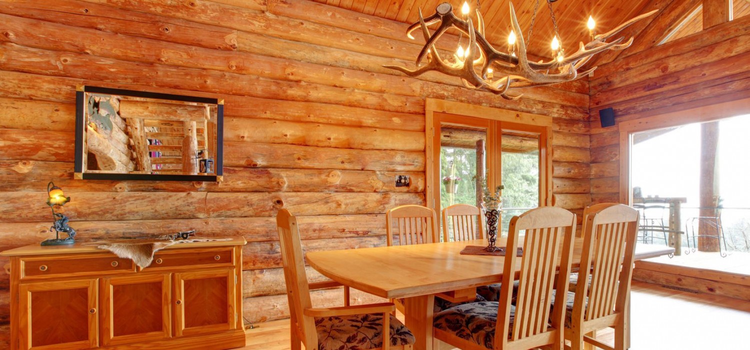 Log-walled dining room with timber ceiling and doors opening to a deck
